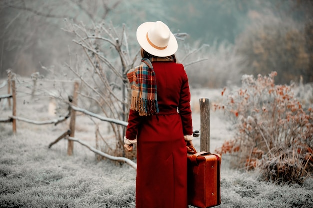 Mujer de abrigo rojo y sombrero con maleta en campo nevado