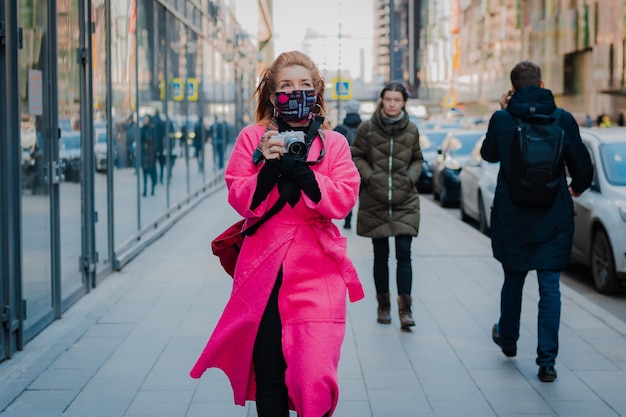 La mujer con un abrigo rosa brillante es una turista con una cámara en un elegante y glamoroso traje protector de moda...