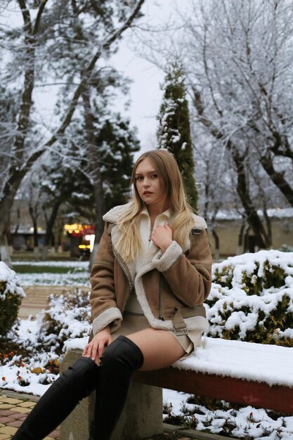 una mujer con un abrigo se sienta en un banco en la nieve
