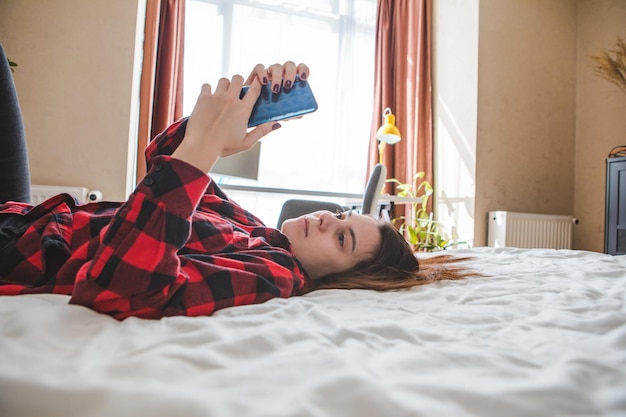 Mujer aburrida acostada en la cama con teléfono celular