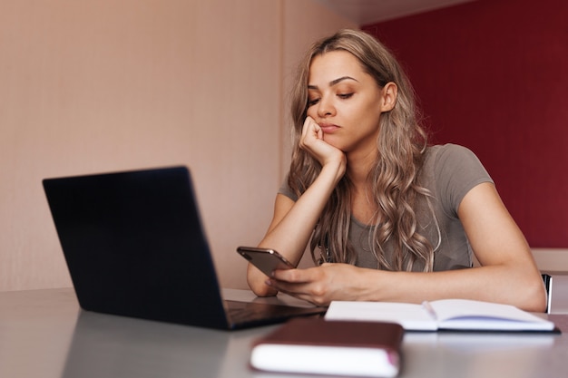 Mujer aburrida con teléfono móvil mientras se toma un descanso del trabajo