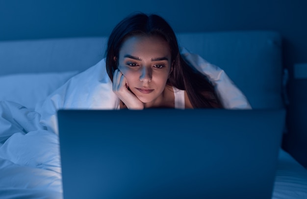 Mujer aburrida viendo la película en la cama por la noche