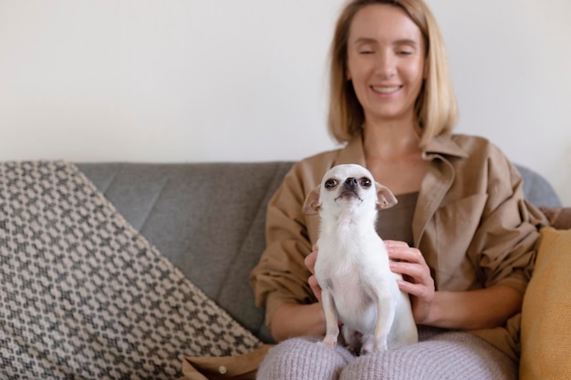 Mujer acaricia a un perro pequeño sentado en el sofá