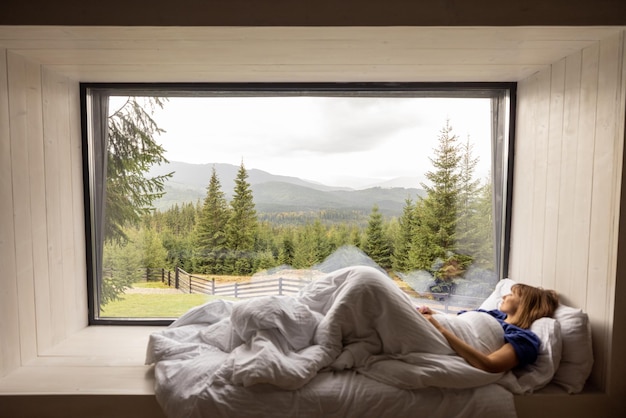 Mujer acostada en el alféizar de la ventana con una gran vista de las montañas