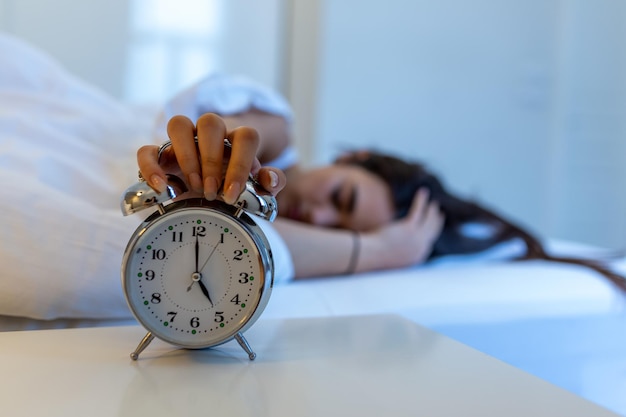 Mujer acostada en la cama apagando un despertador por la mañana a las 5 a.m. La mano apaga el despertador despertándose a la mañana niña apaga el despertador despertándose por la mañana de una llamada