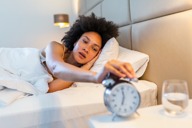 Mujer acostada en la cama apagar un despertador en la mañana a las 7 am.