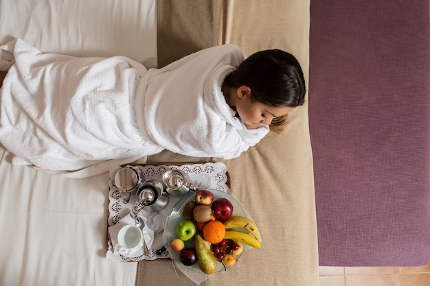 Mujer acostada en la cama cerca de un plato de frutas