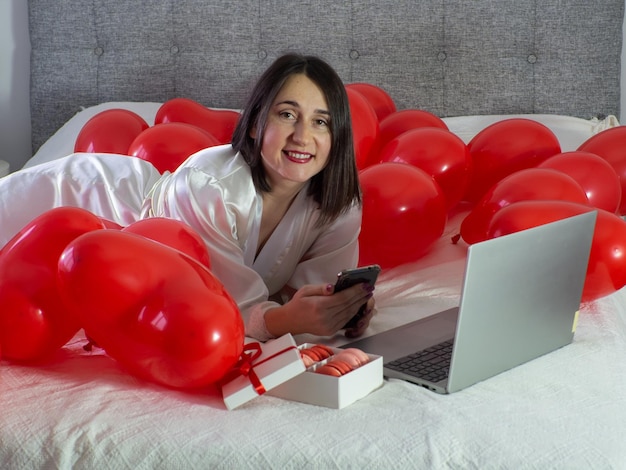 Mujer acostada en la cama con globos rojos para la fiesta del Día de San Valentín