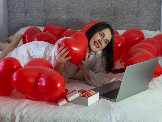Mujer acostada en la cama con globos rojos para la fiesta del Día de San Valentín