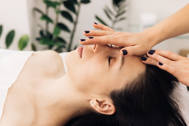 Mujer acostada en la cama de spa obtener tratamiento de masaje facial con aceite esencial de aroma cuidado de la piel de masaje