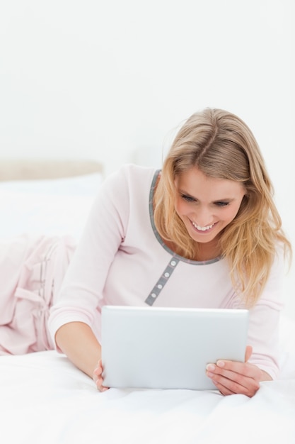 Mujer acostada en la cama, tablet pc en la mano y sonriendo
