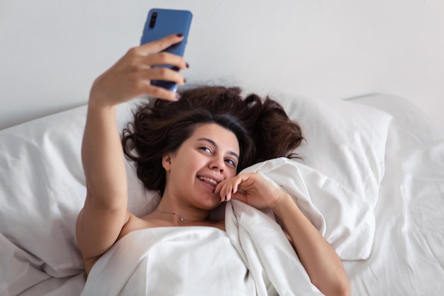 Mujer acostada en la cama tomando selfie por teléfono