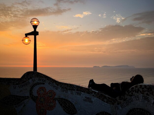 Mujer acostada en la pared de contención por la luz de la calle iluminada contra el cielo al atardecer