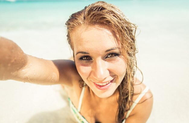 Mujer acostada sobre arena blanca y tomando selfie