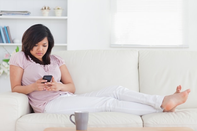 Mujer acostada en un sofá mientras sostiene un teléfono