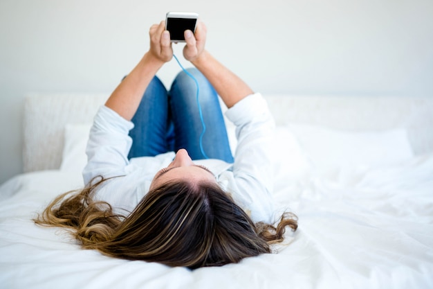 Mujer acostada en su cama escuchando música en su teléfono