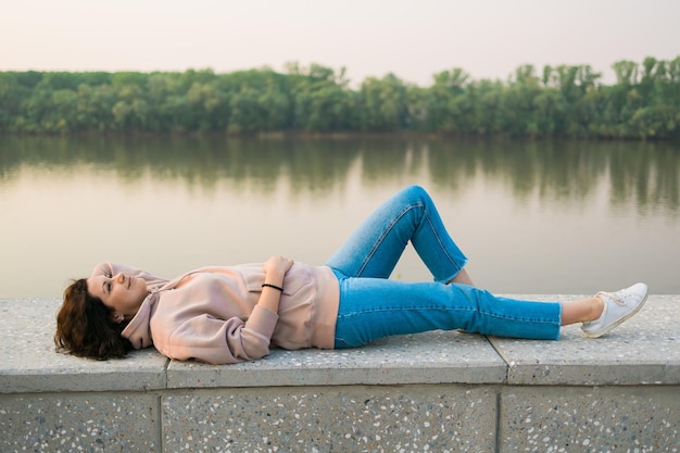 Mujer acostada en el terraplén junto al lago o río en el concepto de soñador y relax del parque de la ciudad