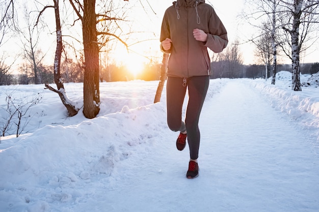 Mujer activa para correr al aire libre en invierno. Persona de sexo femenino que corre a lo largo de la carretera nevada en un hermoso día frío