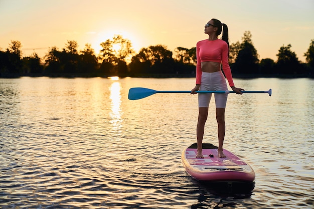 Mujer activa flotando sobre tabla de sup con remo