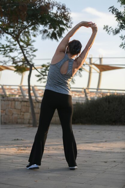 Mujer activa de mediana edad haciendo estiramientos y jogging al aire libre al atardecer