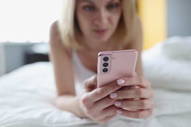 La mujer se acuesta en la cama y mira el primer plano del teléfono inteligente