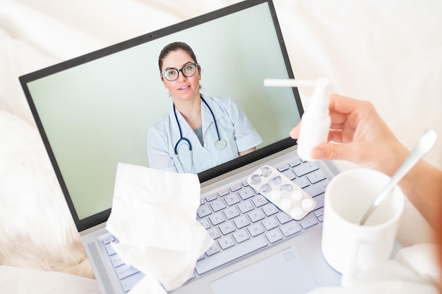 Una mujer se acuesta en la cama y sostiene un spray para el dolor de garganta Un médico amigable habla con un paciente enfermo por enlace de video Terapeuta en la pantalla de una computadora portátil Consulta médica en línea durante la cuarentena