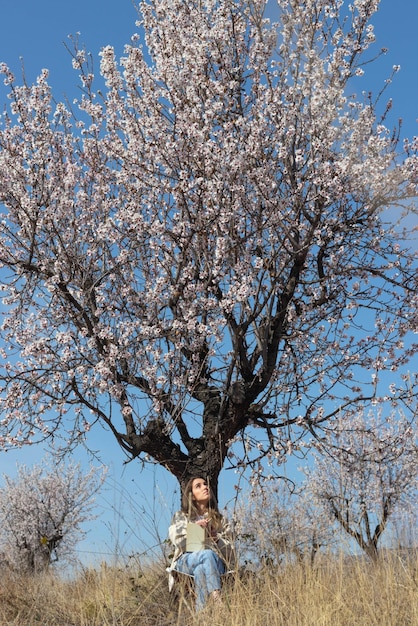 Mujer admirando el hermoso paisaje mientras se sienta debajo de un árbol en un parque