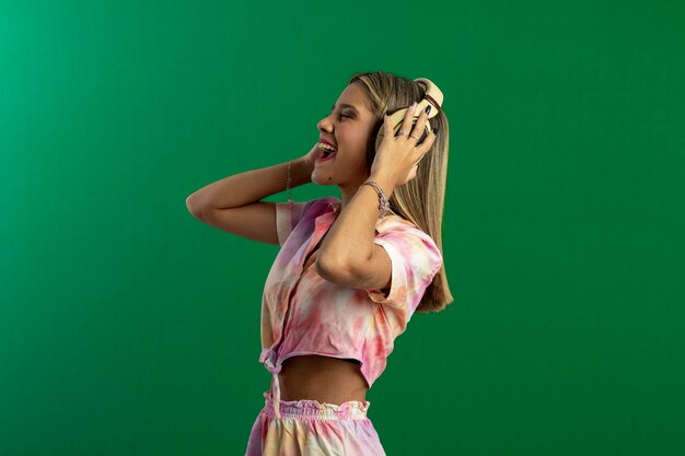 Mujer adolescente en foto de estudio con fondo verde haciendo poses y expresiones faciales y con auriculares