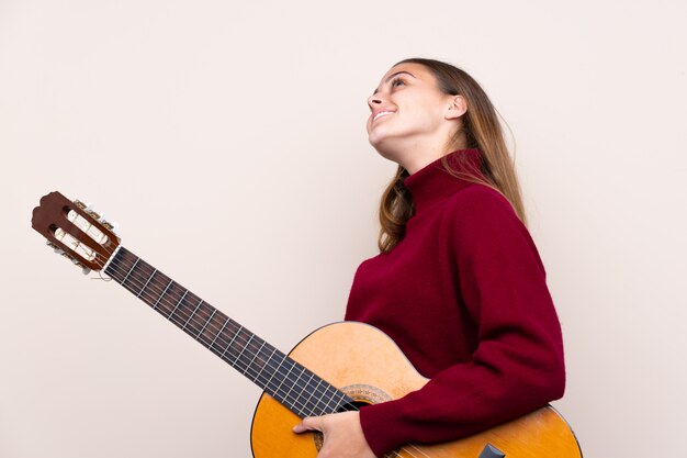 Mujer adolescente con guitarra sobre pared aislada mirando hacia arriba mientras sonríe