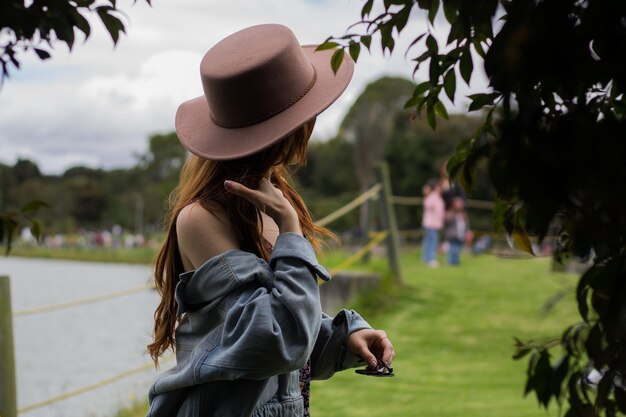 Mujer adolescente joven con un sombrero sentada en la hierba cerca del lago río meditando relajante