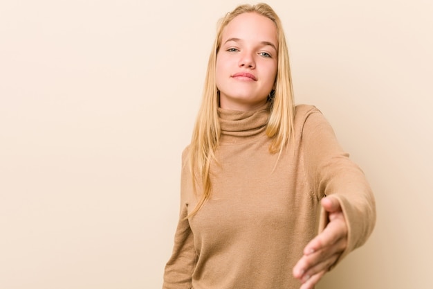 Mujer adolescente linda y natural estirando la mano a la cámara en gesto de saludo.