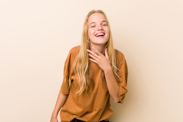 La mujer adolescente linda y natural se ríe a carcajadas manteniendo la mano en el pecho.