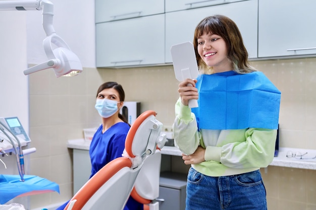 Mujer adolescente mirando dientes sanos en el espejo en el consultorio dental