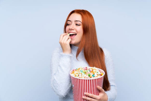 Mujer adolescente pelirroja sosteniendo un gran cubo de palomitas de maíz