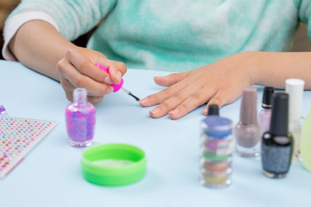 Mujer adolescente pintándose las uñas en casa con suministros de uñas en la mesa