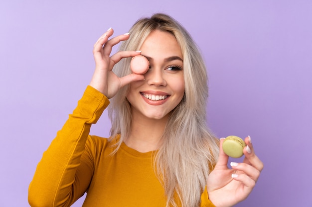 Mujer adolescente sobre pared púrpura aislada con coloridos macarons franceses