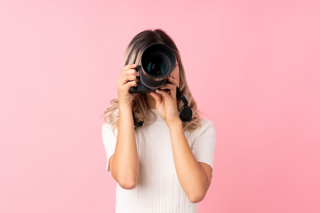 Mujer adolescente sobre rosa aislado con una cámara profesional