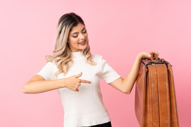 Mujer adolescente sobre rosa aislado sosteniendo un maletín vintage