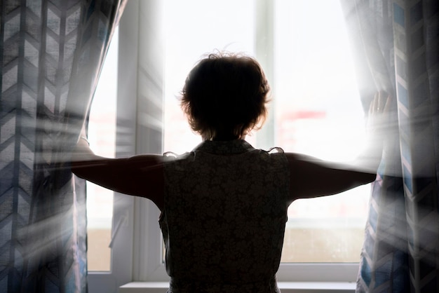 Mujer adulta abre las cortinas de la ventana esperando el día futuro