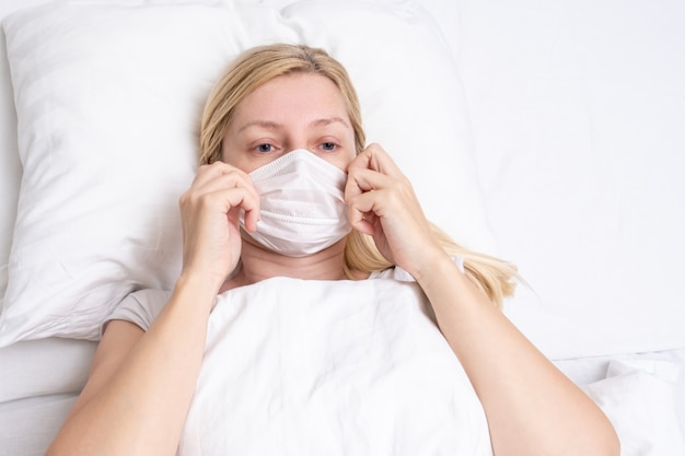 Foto mujer adulta acostada en la cama con gripe, resfriado y fiebre, está enferma y usa mascarilla