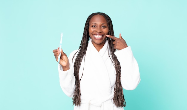 Mujer adulta afroamericana negra con bata de baño y sosteniendo un cepillo de dientes