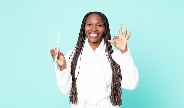 Mujer adulta afroamericana negra con bata de baño y sosteniendo un cepillo de dientes