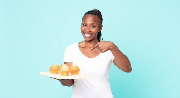 Mujer adulta afroamericana negra sosteniendo una bandeja de muffins