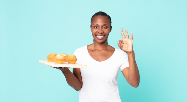 Mujer adulta afroamericana negra sosteniendo una bandeja de muffins