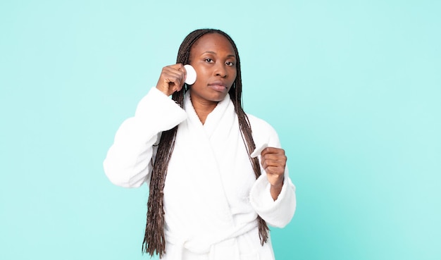 Mujer adulta afroamericana negra vistiendo albornoz y sosteniendo un algodón de limpieza facial
