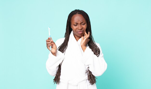 Mujer adulta afroamericana negra vistiendo albornoz y sosteniendo un cepillo de dientes