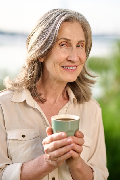 Mujer adulta alegre con taza en la naturaleza