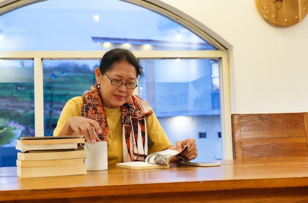 Una mujer adulta asiática disfruta leyendo en el comedor mientras toma un té caliente