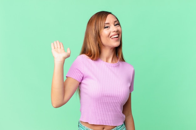 Mujer adulta bonita sonriendo felizmente, saludando con la mano, dándote la bienvenida y saludándote