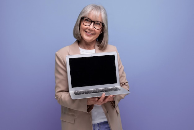 Mujer adulta confiada en una chaqueta con una computadora portátil en un fondo brillante con espacio de copia